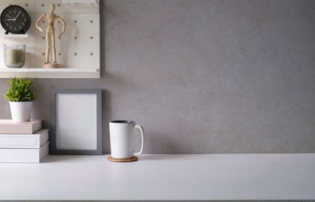 Home office desk with supplies, picture frame, house plant and coffee cup on white table.