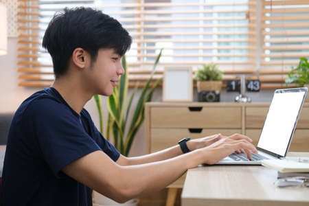Smiling handsome asian man sitting on floor in living room and using laptop computer.の写真素材