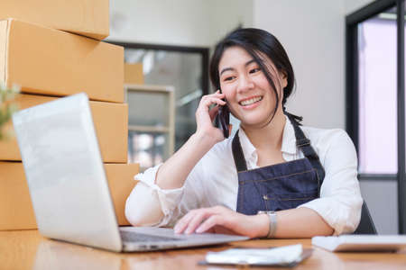 Startup small business entrepreneur owner talking on mobile phone and checking online purchase on computer.の写真素材