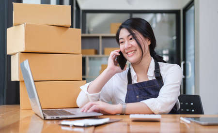 Young female online seller confirming orders from customer on mobile phone.の写真素材