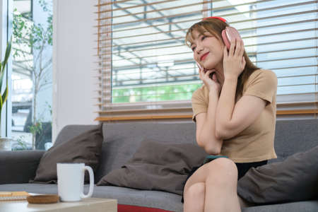 Pretty young woman listening to music with wireless headphone and relaxing at home.の写真素材