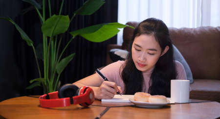 Concentrated young woman doing homework while sitting floor in living room.の写真素材