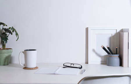 Office desk with picture frame, coffee cup, houseplant and supplies on white table. Copy space for your advertise text.の写真素材