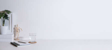 Home office desk with books, glass of water and potted plant on white table. Copy space for your text.の写真素材