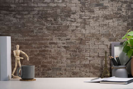 Creative workspace with blank poster frame, coffee cup, books and flower pot on white table with...