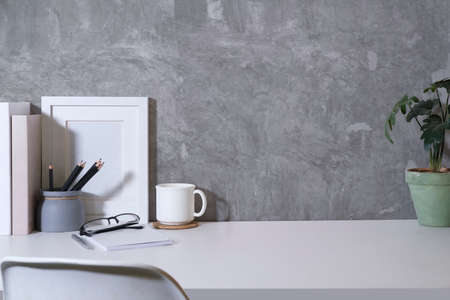 Stylish workplace with books, coffee cup, picture frame and potted plant on white table. Copy space...