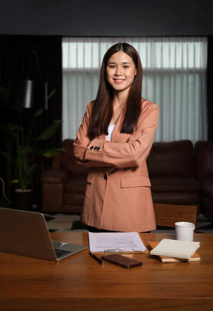 Confident businesswoman standing with arms crossed in contemporary office and smiling to camera.の写真素材