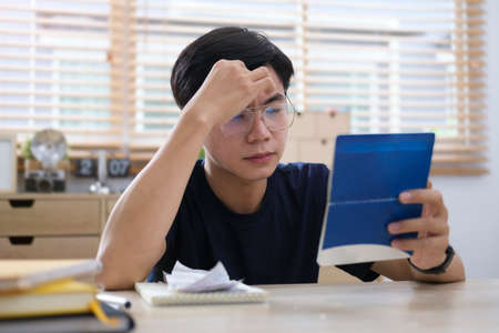 Worried asian man calculating bills, upset about money problem, manage household finances at home.の写真素材