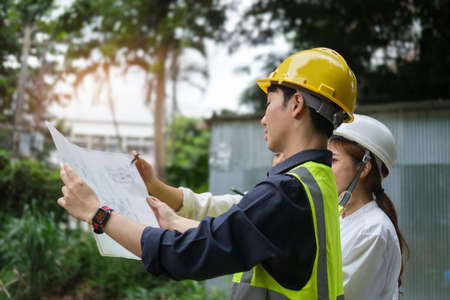 Young civil engineers wearing  safety helmets and vast working with blueprint, inspecting new construction site.の写真素材