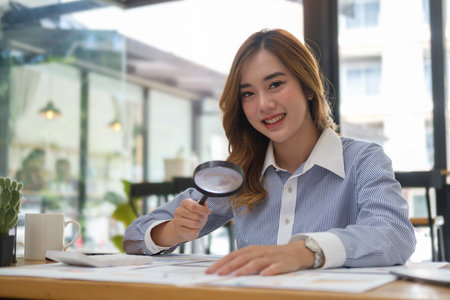 Businesswoman examining documents with a magnifying glass at her office desk.の写真素材
