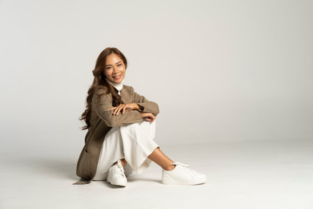 Stylish beautiful woman in brown jacket sitting on white background. Beauty and fashion in autumn.の写真素材