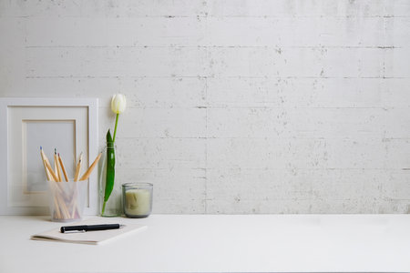 Feminine workplace with picture frame, candle and notebook on white table. Copy space for your text.の写真素材