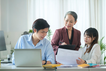Smiling senior business woman discuss financial statistics,  reviewing reports with young businesspeople in office.の写真素材