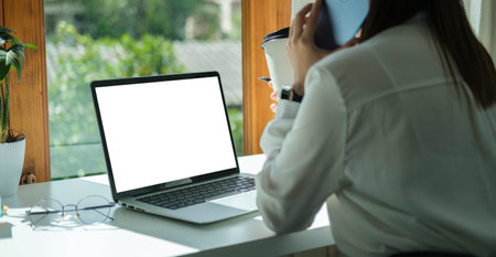 Side view of young woman office worker sitting front of laptop and talking on mobile phone.の写真素材