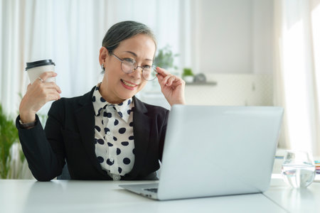 Successful senior female entrepreneur wearing glasses checking online news or email on her laptop.の写真素材