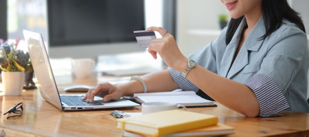 Smiling young woman holding credit card and using laptop for online banking transaction, e-commerce.の写真素材