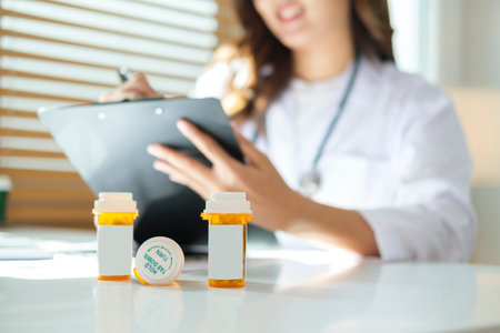 Plastic medical bottles on a white table against female doctor writing prescription to patient in background.の写真素材