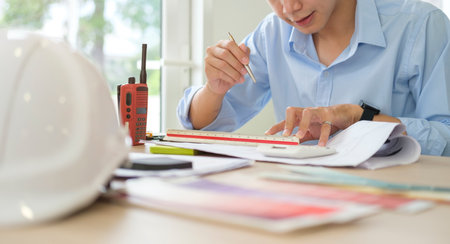 Handsome male architect working with blueprints, inspecting architectural plan at workplace.