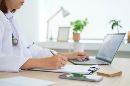 Cropped shot of doctor in white uniform using laptop and filling up medical recommendations in a clinic office.の写真素材