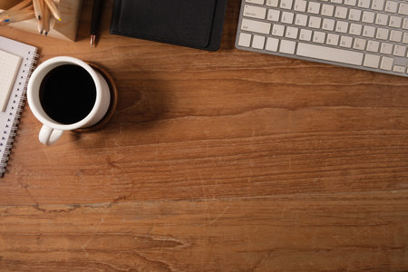 Top view of simple workplace with cup of coffee, pencils and notepad on wooden table. Top view with...