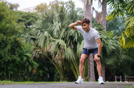 Tired athletic man in sports wear taking a rest after morning workout or running in public park....