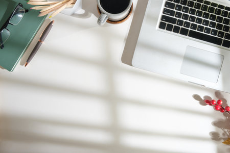 Top view of laptop, coffee cup, notepad and pencil holder on white office desk. Copy space for your...