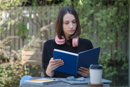 Beautiful young woman sitting in garden and relaxing with book on a cozy winter dayの写真素材