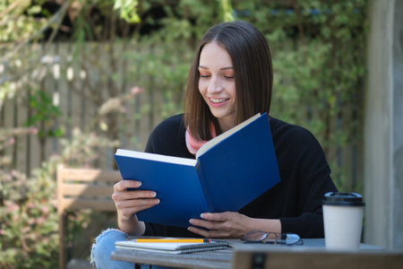 Pleased young woman in warm sweater relaxing outdoor and reading book.の写真素材