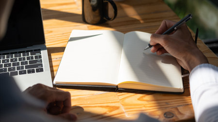 Close up view of businessman using laptop and making notes on notepad with with sunlight.
