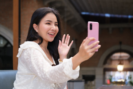 Charming asian woman waving hand, looking at smartphone web camera, starting video call distant...