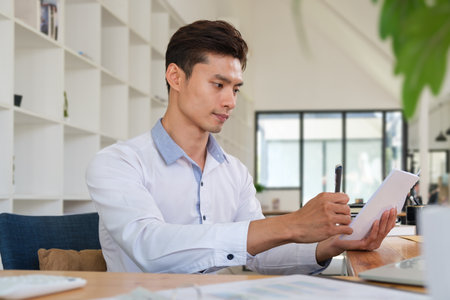 Young asian man office worker writing information on notepad, working in modern office.の写真素材