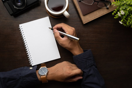 Businessman hand holding pen, writing on empty notepad. Above view, blank screen for your advertise design.の写真素材