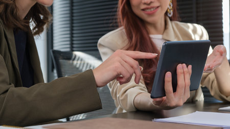 Smiling female office worker working, explaining online information to her colleague.の写真素材