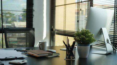 Office desk with with computer, office supplies and houseplant in modern office interiorの写真素材