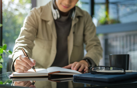 Young man freelancer sitting at table in outdoor cafe and writing in notebook.の写真素材
