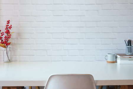 Home office desk with books, cup of coffee and stationery on white table against brick wall. Copy space for your text.の写真素材