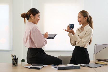 Indian attractive positive woman talking with colleague during coffee break at coworking areaの写真素材
