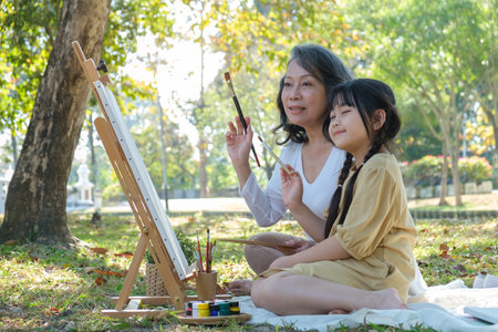 Joyful little girl and middle aged grandma painting on canvas, enjoy leisure weekend outdoor together.の写真素材