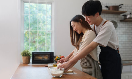 Beautiful young couple preparing meal, making fresh dough for breakfast in the kitchen .の写真素材