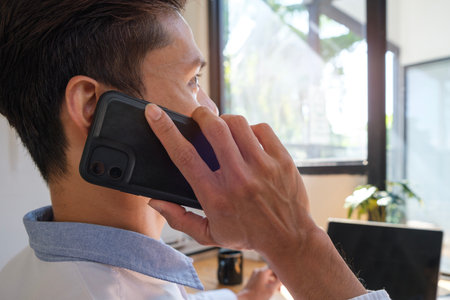 Millennial asian businessman sitting in modern office and talking on mobile phone.