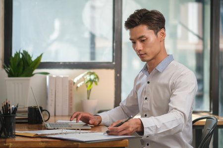 Start up businessman writing new idea on notepad and using laptop in bright modern office.の写真素材