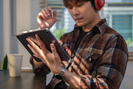 Satisfied millennial man wearing headphone using digital tablet in modern home office.の写真素材