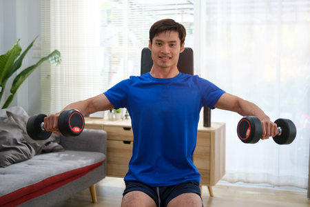 Handsome athletic muscular man lifting dumbbells while sitting on sports bench. Fitness, sport and healthy lifestyle concept.の写真素材