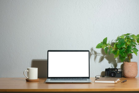 Laptop computer with empty screen, coffee cup, houseplant and camera on wooden table.の写真素材