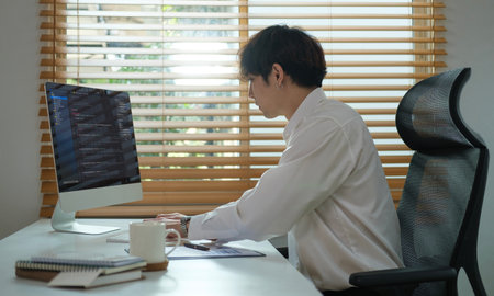 Focused young male programmer working on computer software, sitting at desk and writing codes.の写真素材