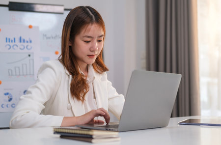 Focused female manager typing on laptop keyboard, checking email, taking part in online meeting at office desk.の写真素材