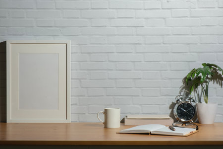White empty frame mock up coffee cup, notebook and potted plant on wooden table in bright room of modern house.の写真素材