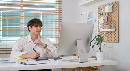 Smiling young asian man UX designer working with graphic tablet and developing a new app design at office.の写真素材