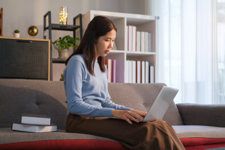 Beautiful female freelancer sitting on couch in living room and using laptop. Distance learning online education and remote working.の写真素材