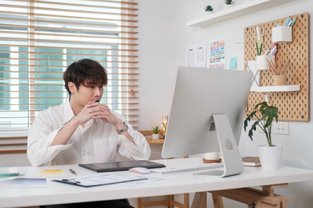 Image of handsome Asian male entrepreneur in white shirt looking at computer screen, working in modern office.の写真素材